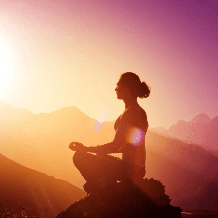 Woman meditating with pink sunset on mountain top